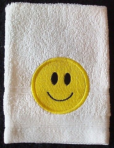 A picture of a white hand towel with an embroidered yellow smiley face.