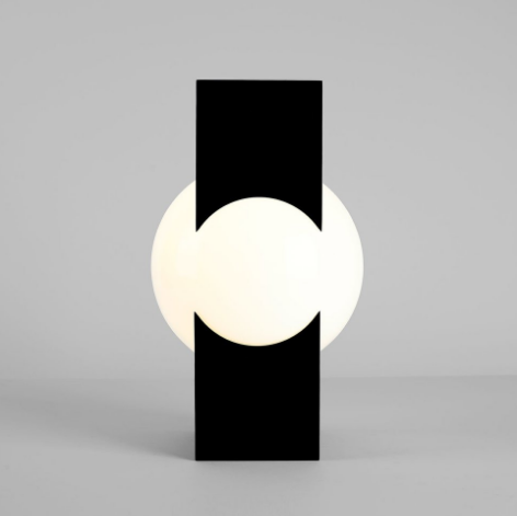 A picture of an artistically designed black rectangular lamp with a soft white circle of light in the center.